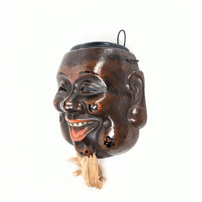 Vue de trois quarts d’un masque traditionnel japonais de Daikoku, objet d’art en laque sèche avec système de suspension au revers.