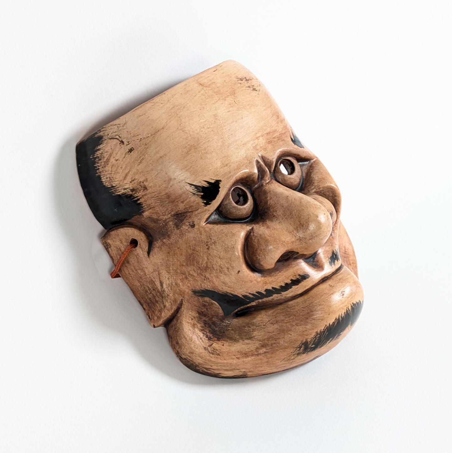 Vue de profil d’un masque démon japonais Beshimi en céramique, nez proéminent, bouche fermée et expression surnaturelle