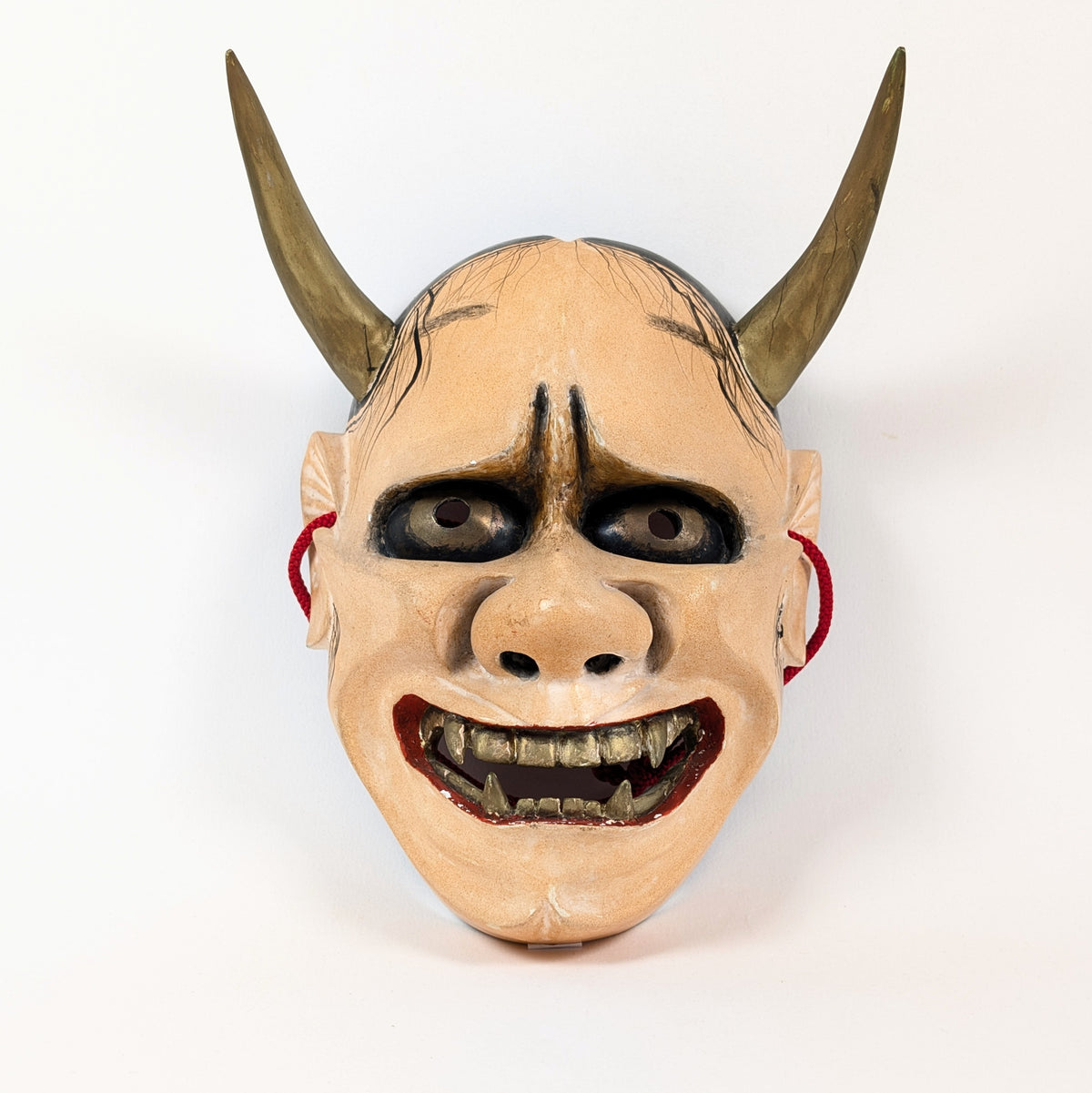 Portrait frontal d'un masque Hannya, femme-démon du théâtre Nô, aux arcades sombres et crocs dorés.