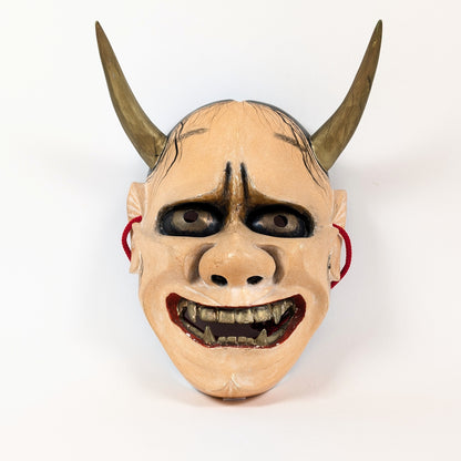 Portrait frontal d'un masque Hannya, femme-démon du théâtre Nô, aux arcades sombres et crocs dorés.