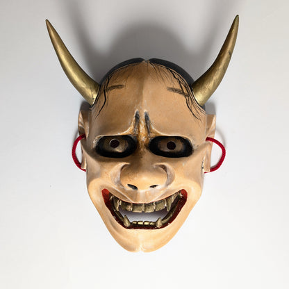 Masque Hannya de l'époque Shōwa vu de face, avec deux longues cornes dorées projetant leur ombre sur le fond clair.