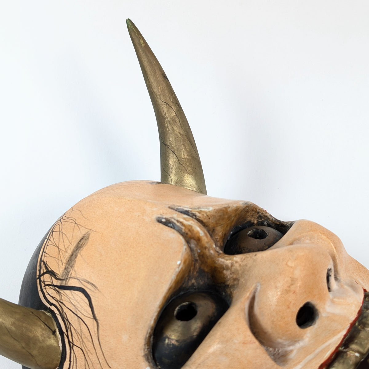 Détail du visage d'un masque Hannya vu en contre-plongée, avec yeux à reflets métalliques et cornes dorées.