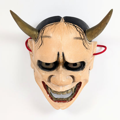 Masque Hannya de théâtre Nô vu en plongée, soulignant le regard abaissé, les sourcils tourmentés et les crocs.