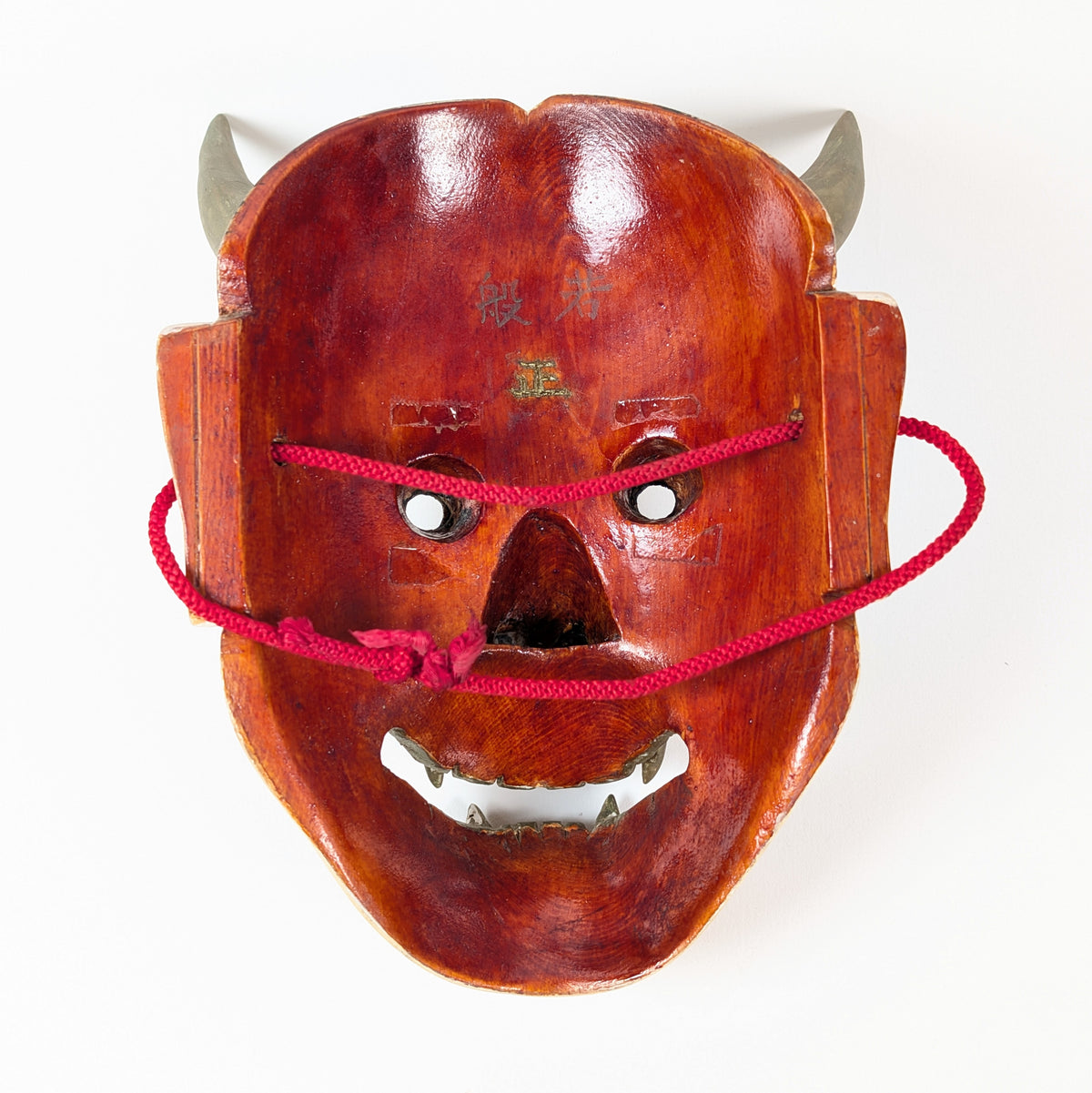 Revers évidé et rouge brillant d'un masque Hannya d'époque Shōwa, avec cordon rouge, inscription 般若 et signature.