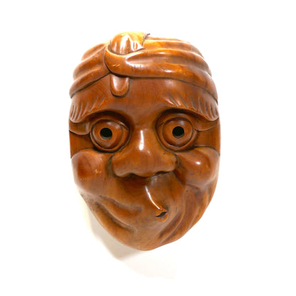 Masque traditionnel Hyottoko vu de biais avec éclairage latéral, accentuant les volumes expressifs du visage.