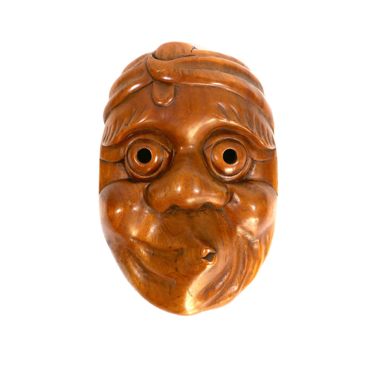 Masque Hyottoko photographié de face sur fond blanc avec lumière directe, mettant en valeur la sculpture et la patine du bois.