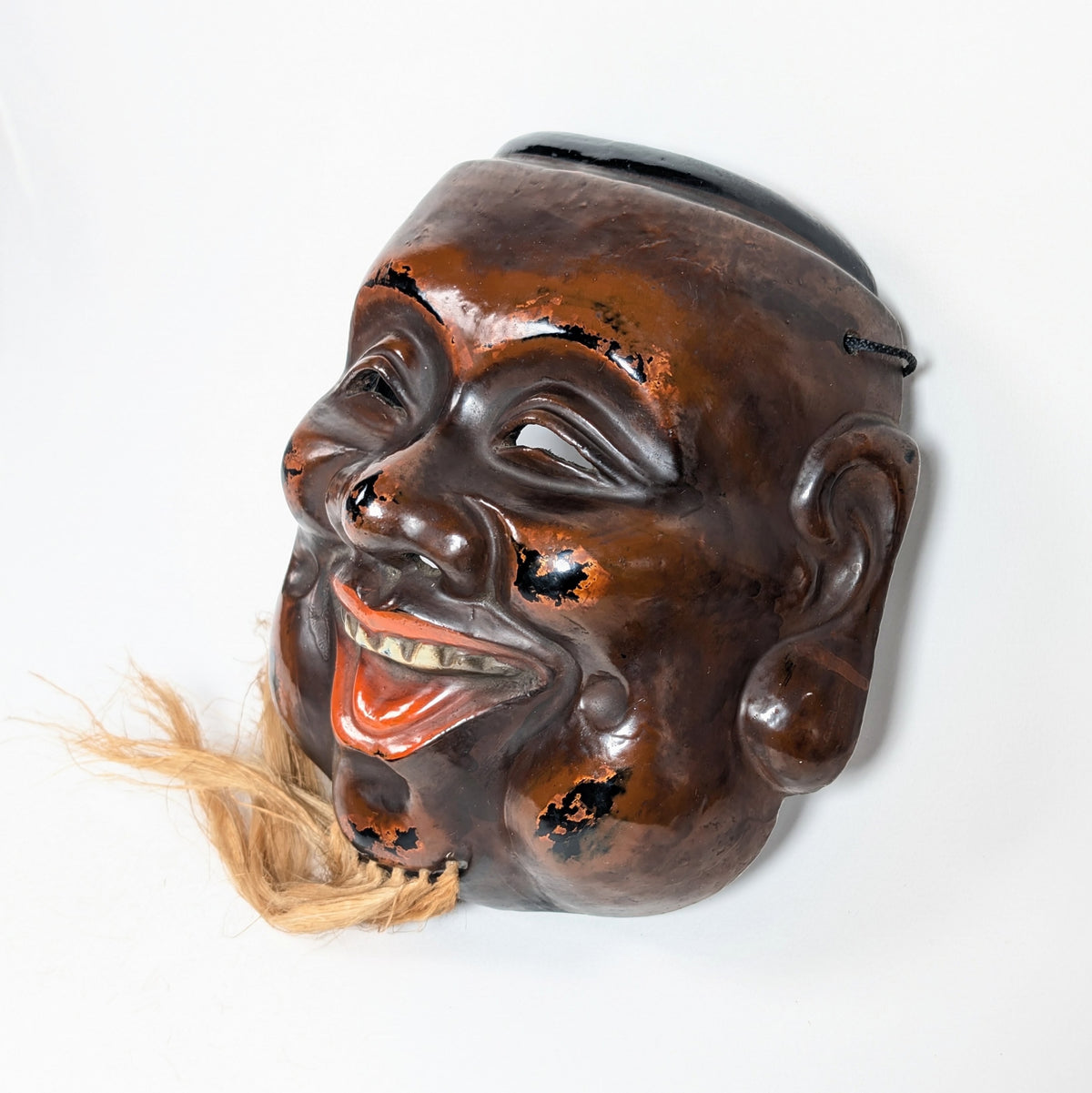 Vue de profil d’un masque japonais de Daikoku montrant son fort relief sculptural, son nez proéminent et sa construction creuse en kanshitsu.
