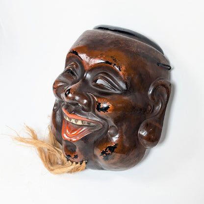 Vue de profil d’un masque japonais de Daikoku montrant son fort relief sculptural, son nez proéminent et sa construction creuse en kanshitsu.