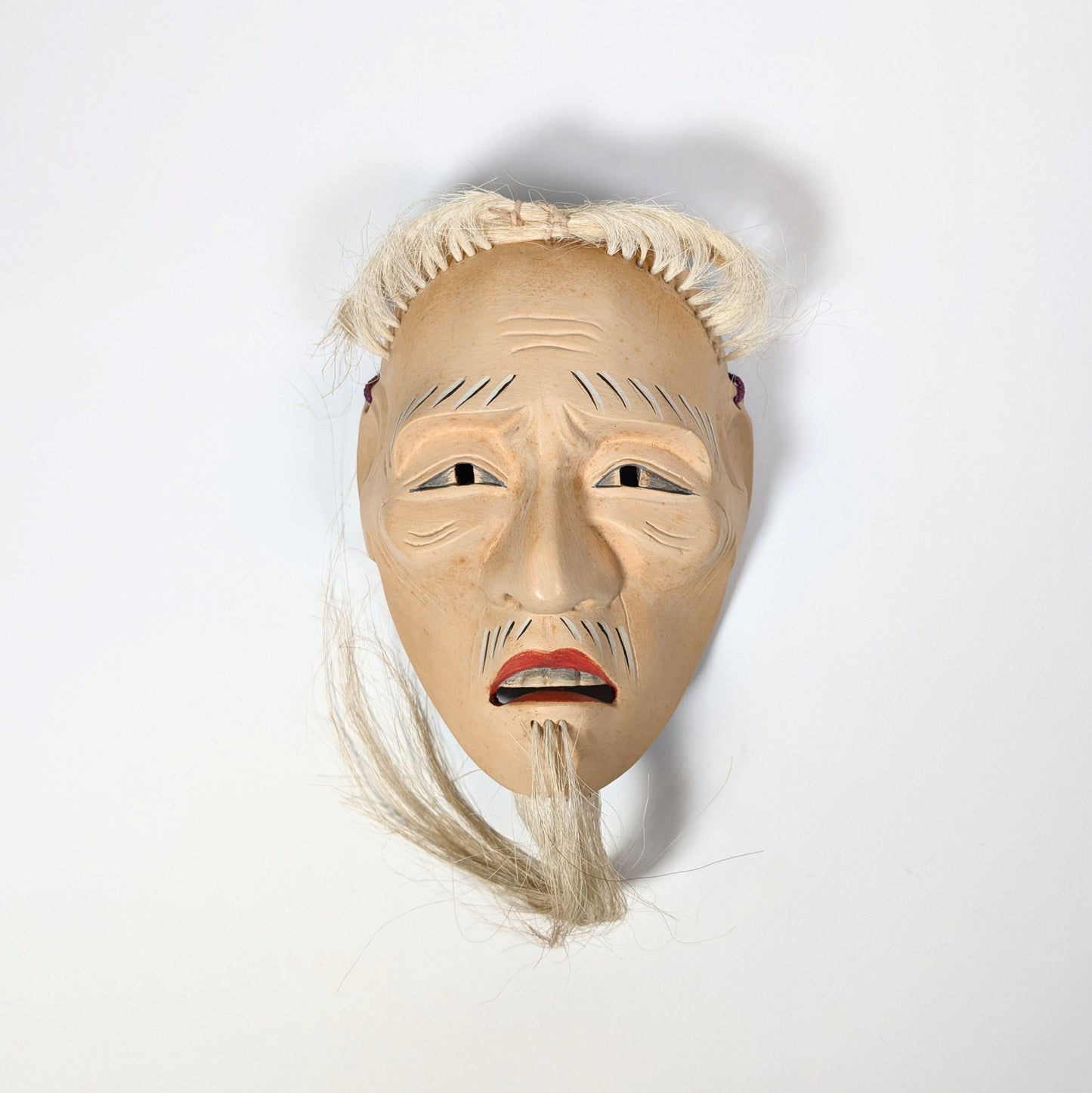 Vue frontale d’un masque japonais de théâtre Nô, nōmen ancien, expression neutre révélée par l’éclairage frontal.