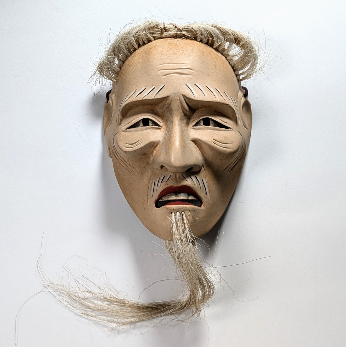 Masque japonais du théâtre Nô vu de face sous lumière zénithale, mettant en valeur les volumes sculptés.