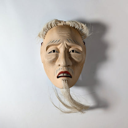 Masque Nô japonais Kōshi-jō vu de face avec éclairage contrasté, accentuant l’expression grave du visage.
