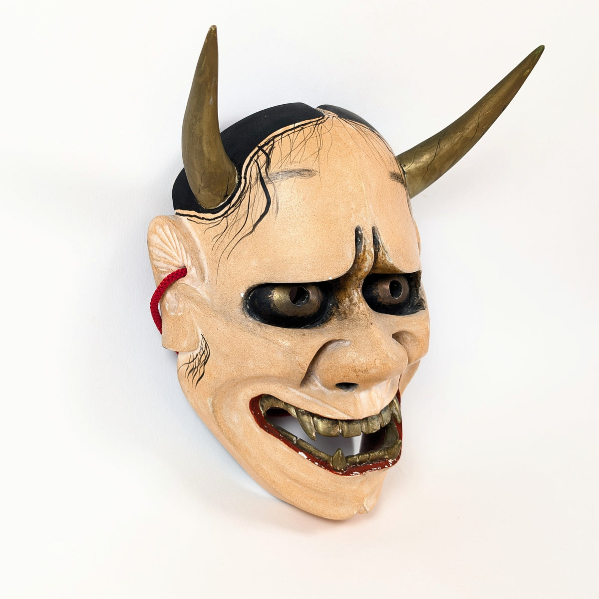 Masque Noh Hannya en bois sculpté, vu de trois quarts, avec front bombé, yeux sombres et dentition dorée.