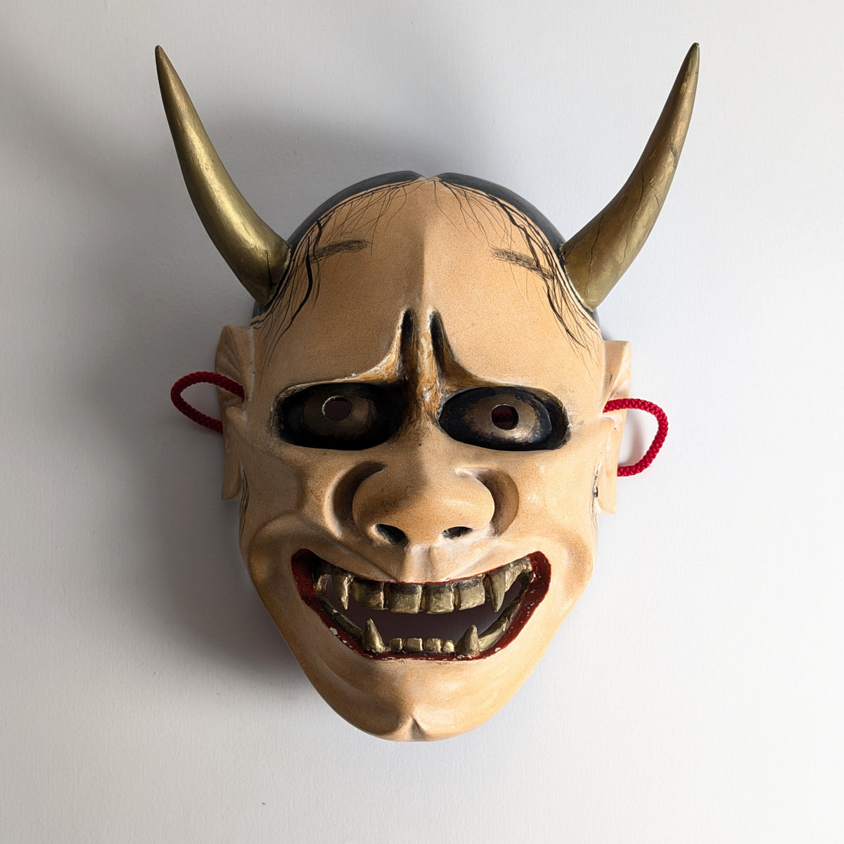 Vue de face du masque Nô Hannya en bois polychrome, éclairé de côté, soulignant ses cornes et son regard sombre.