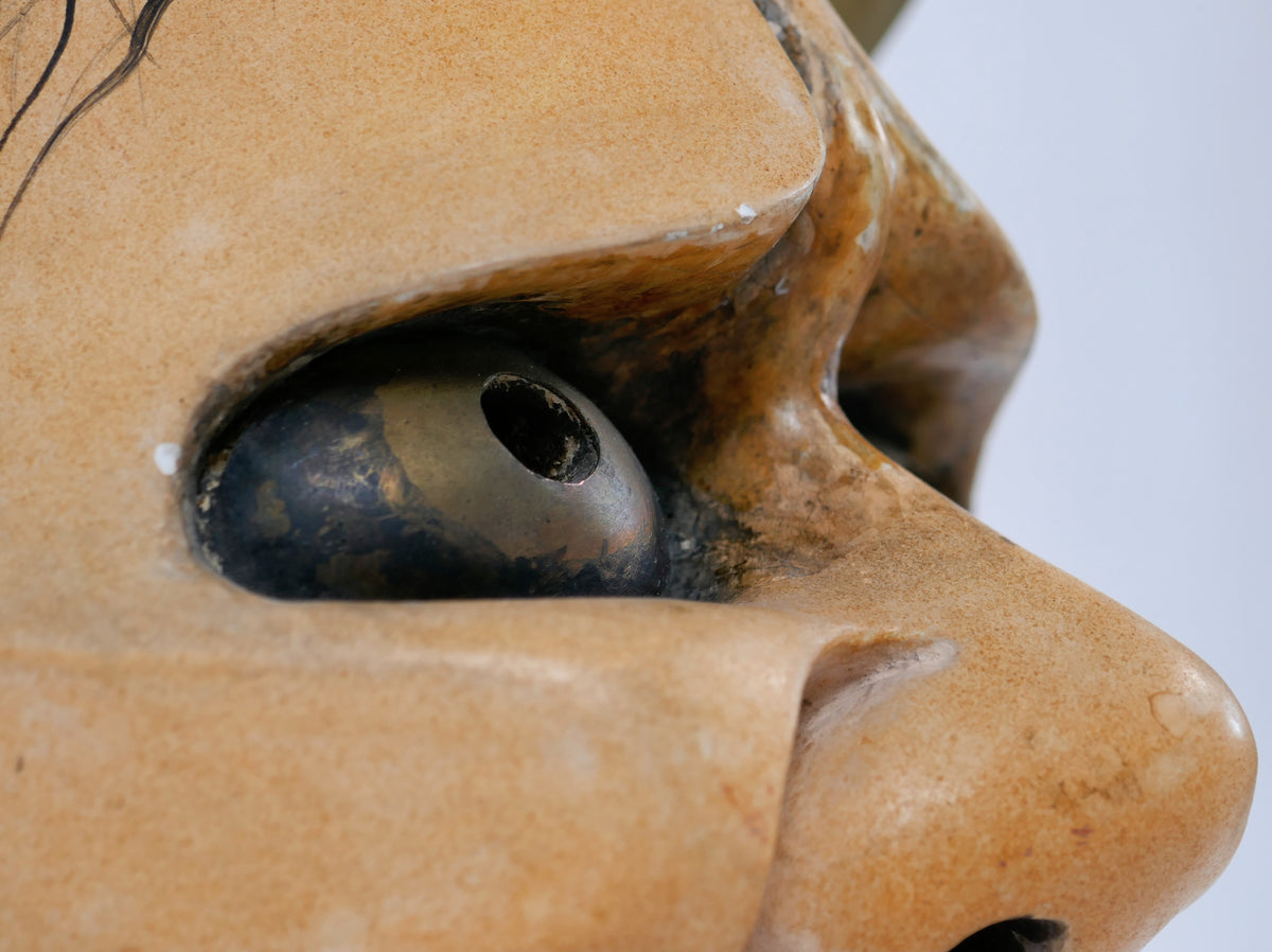 Détail de profil du regard d'un masque Noh japonais Hannya, avec globe à reflets bronze et nez saillant.
