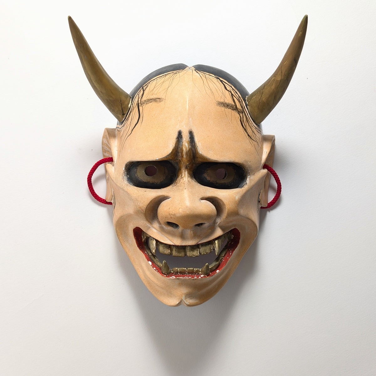 Masque de théâtre Nô Hannya de face : visage ivoire patiné, yeux brun doré et bouche rouge aux dents saillantes.