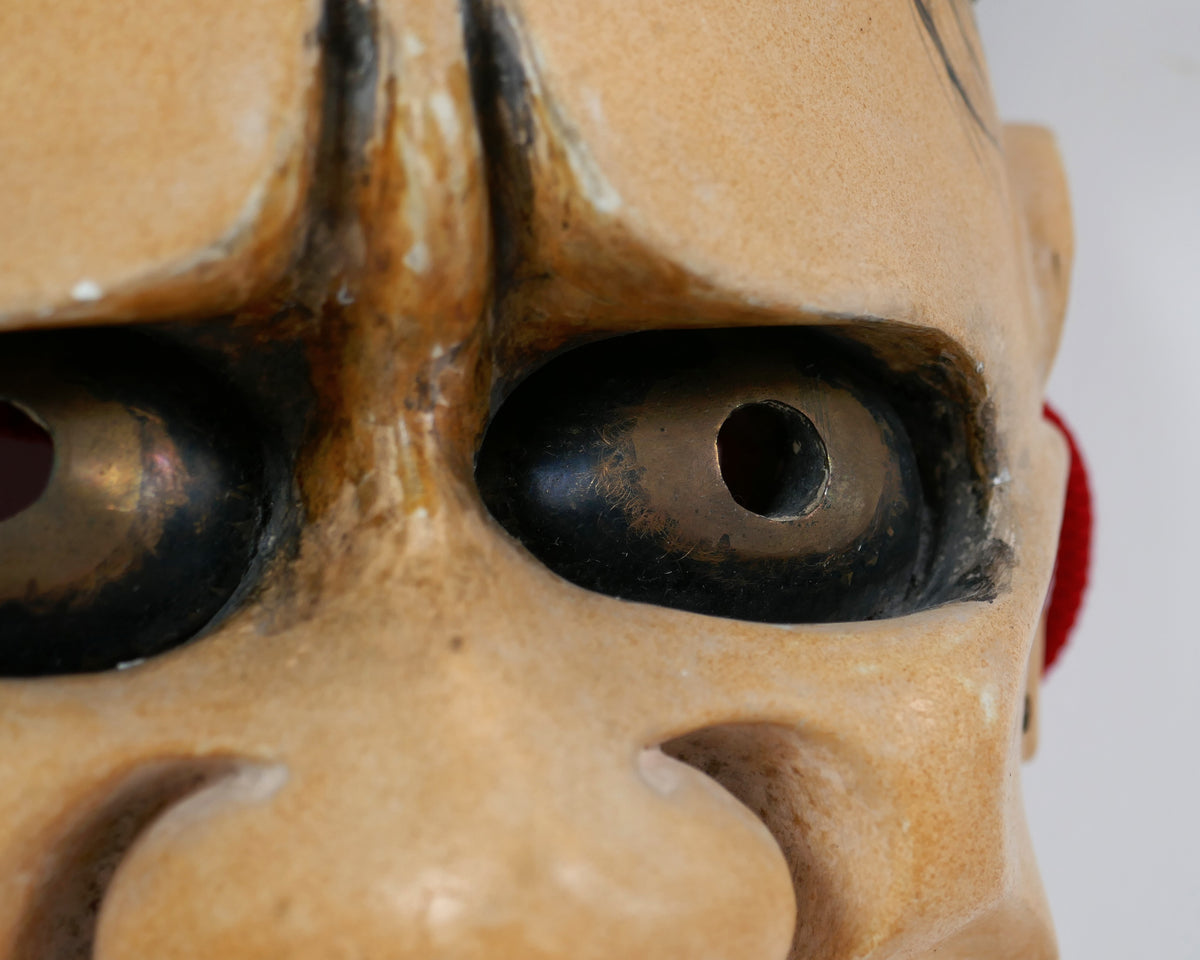Gros plan des yeux à reflets bronze du masque de théâtre Nô Hannya, avec orifices de vision dans les pupilles.