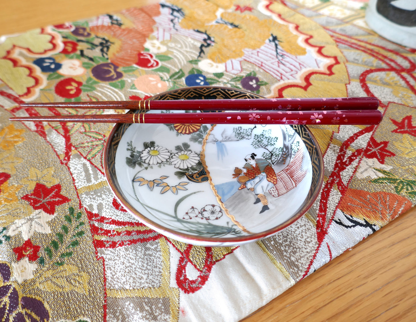 Assiette japonaise Kutani mise en scène avec baguettes rouges sur un obi traditionnel japonais en soie en centre de table