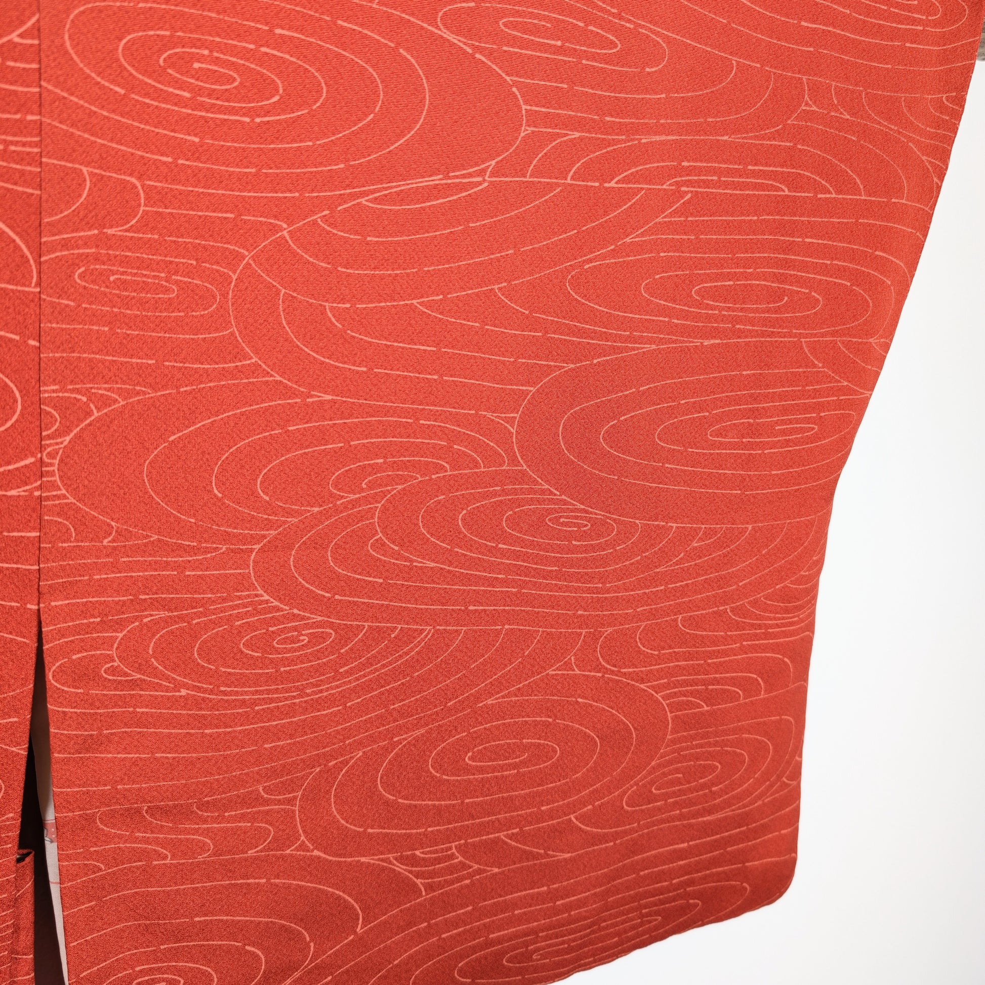 Gros plan sur la soie chirimen orange d’un haori japonais, décor de tourbillons uzumaki et lignes d’eau