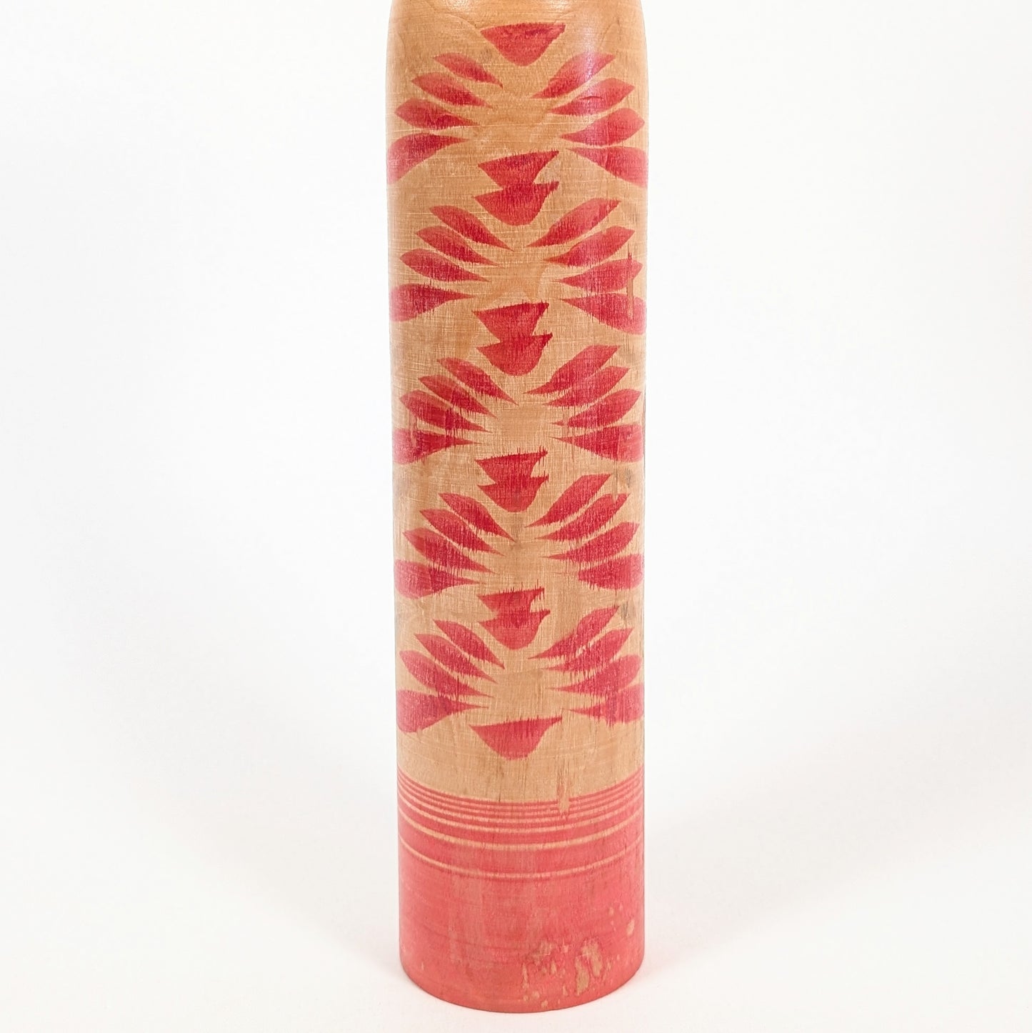 Détail du motif kasane-giku de la kokeshi traditionnelle, composé de chrysanthèmes superposés rouges sur bois naturel.