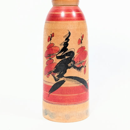 Détail du motif ume sur une kokeshi Yajirō, branches et fleurs de prunier peintes en rouge et noir sur bois naturel