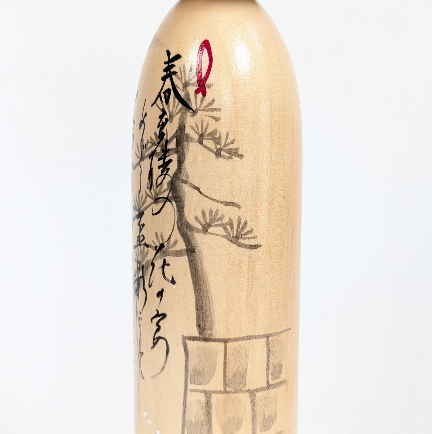Vue rapprochée du pin peint et de la calligraphie sur la shingata kokeshi vintage de Shūhō 秀峰.