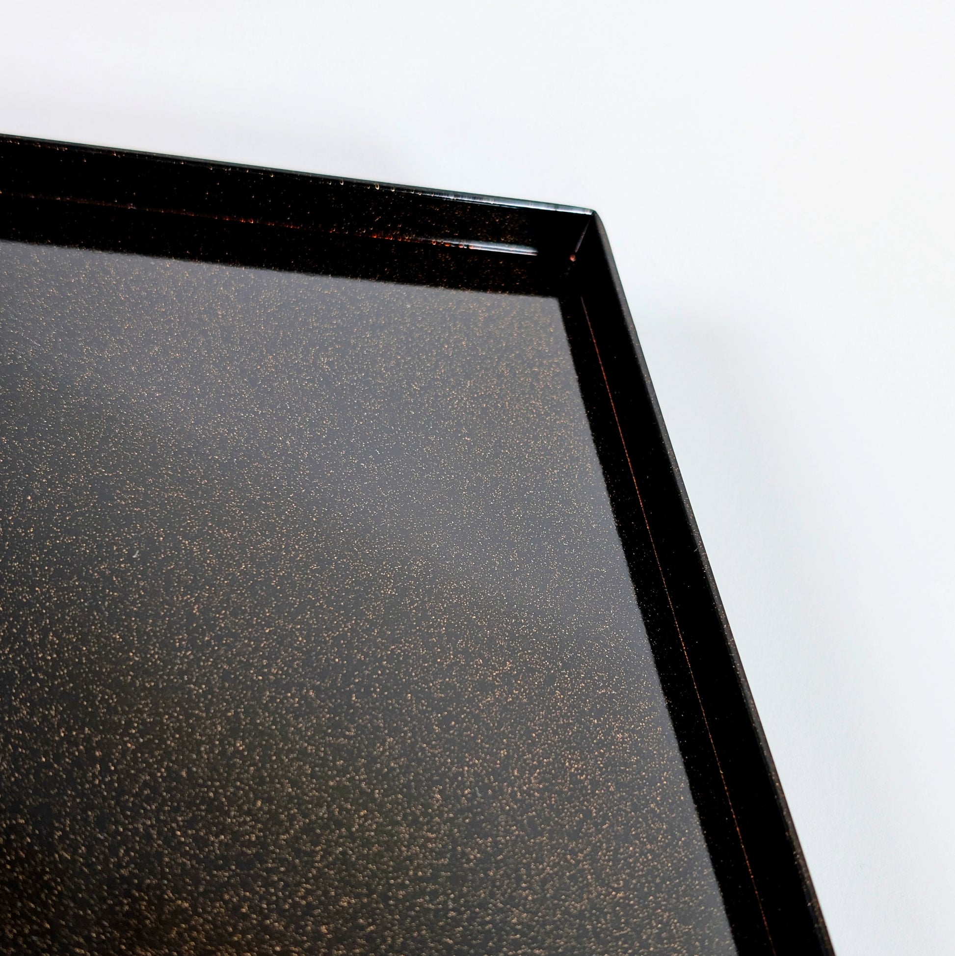 Plateau de boîte en laque noire avec texture nashiji scintillante, vue sur l’angle et le rebord.