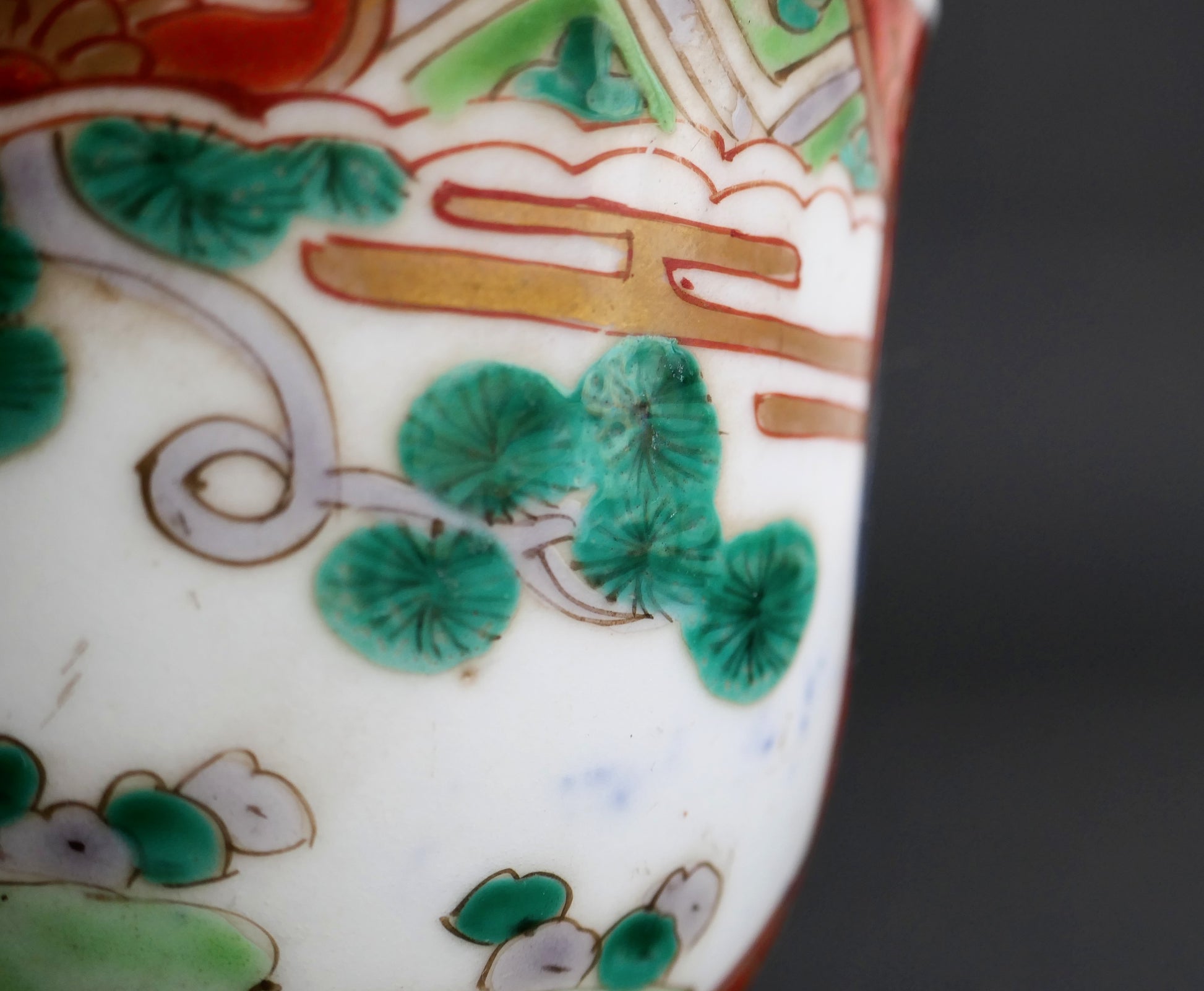 Détail du pin vert, des rehauts dorés et des irrégularités de cuisson sur porcelaine Arita Imari ancienne.