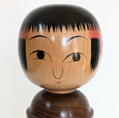 Visage peint à la main d'une kokeshi Oshin par Mamoru Izu, expression douce et stylisée