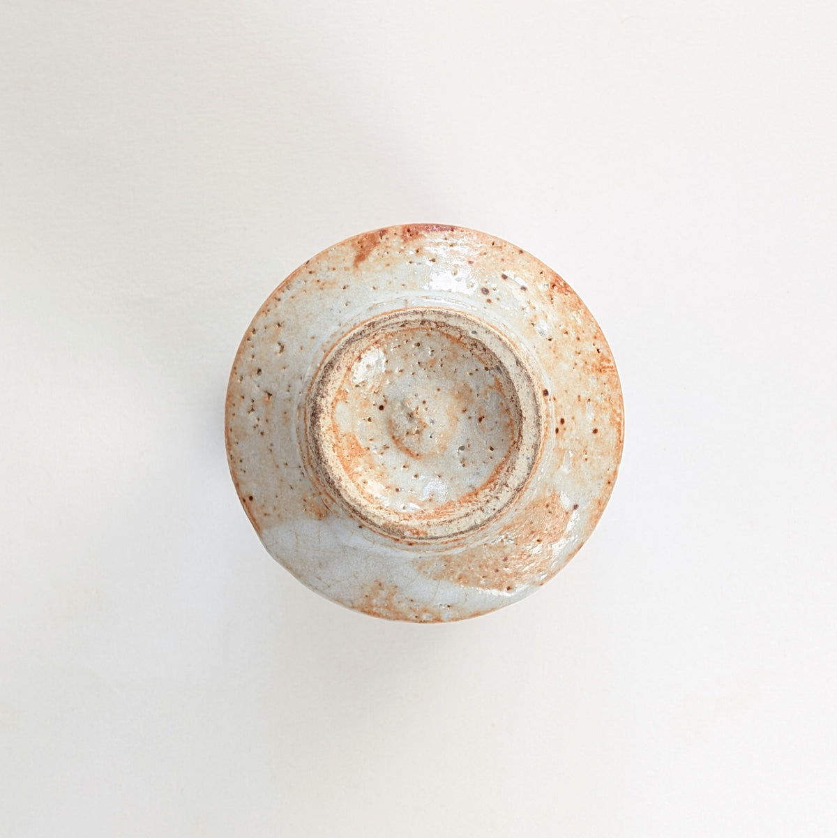 Dessous d'une tasse japonaise en céramique Shino, avec pied circulaire et traces de façonnage au tour.