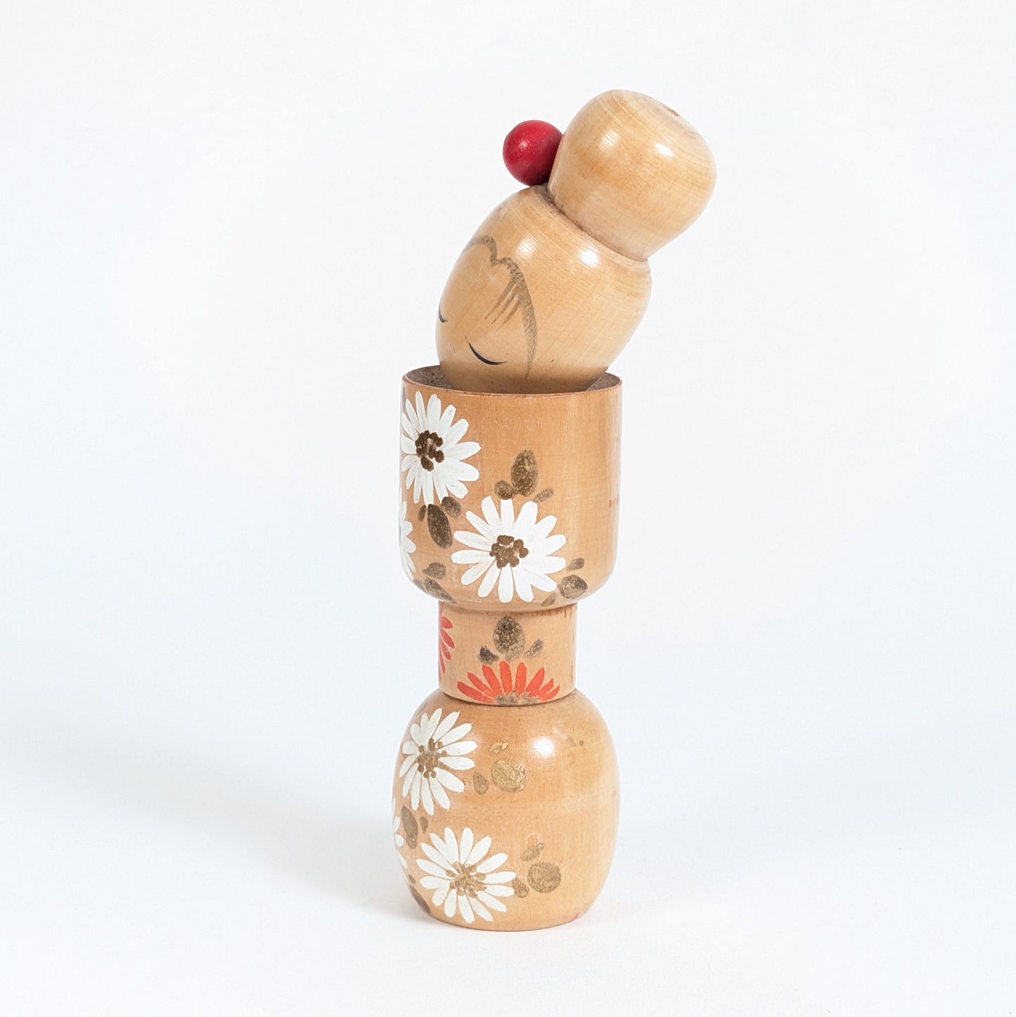 Poupée japonaise en bois par Ishida Tomio, profil d’une kokeshi fleurie aux motifs blancs et orange.