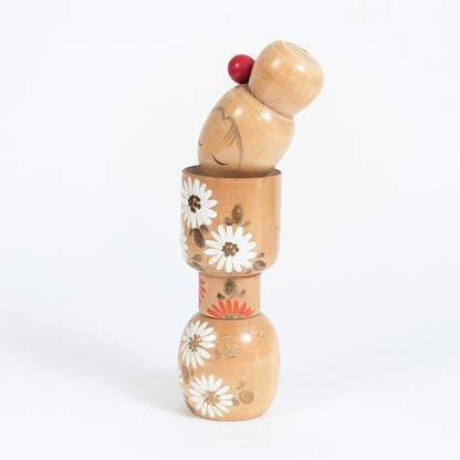 Poupée japonaise en bois par Ishida Tomio, profil d’une kokeshi fleurie aux motifs blancs et orange.