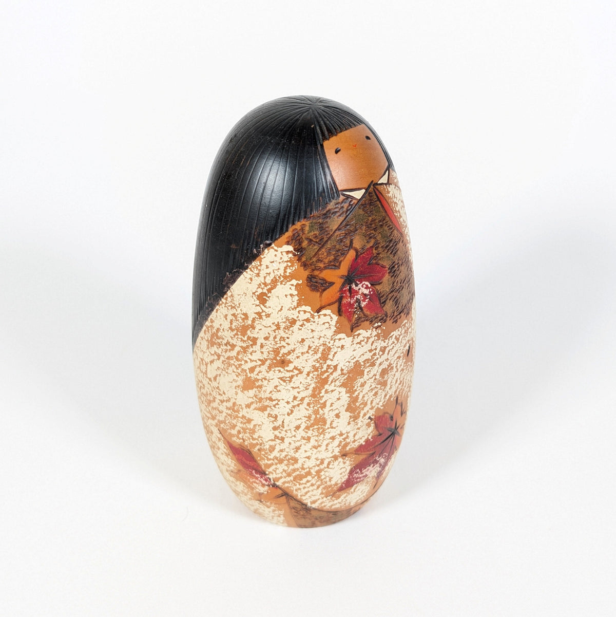 Vue de trois quarts de la poupée kokeshi japonaise en bois, avec chevelure noire sculptée et feuillages momiji sur son kimono.