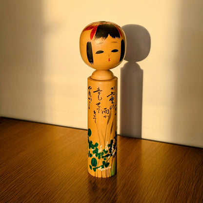 Poupée japonaise en bois kokeshi Usuki Hakuhō illuminée par la lumière dorée du soir, motifs d’automne hagi et susuki, artisanat sosaku omiyage de Sendai