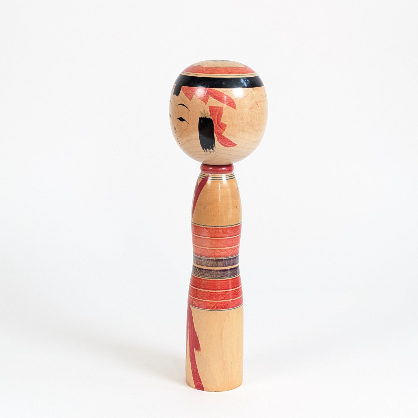 Poupée japonaise en bois de style Yajiro vue de profil, décor rouge, noir et lignes peintes au tour