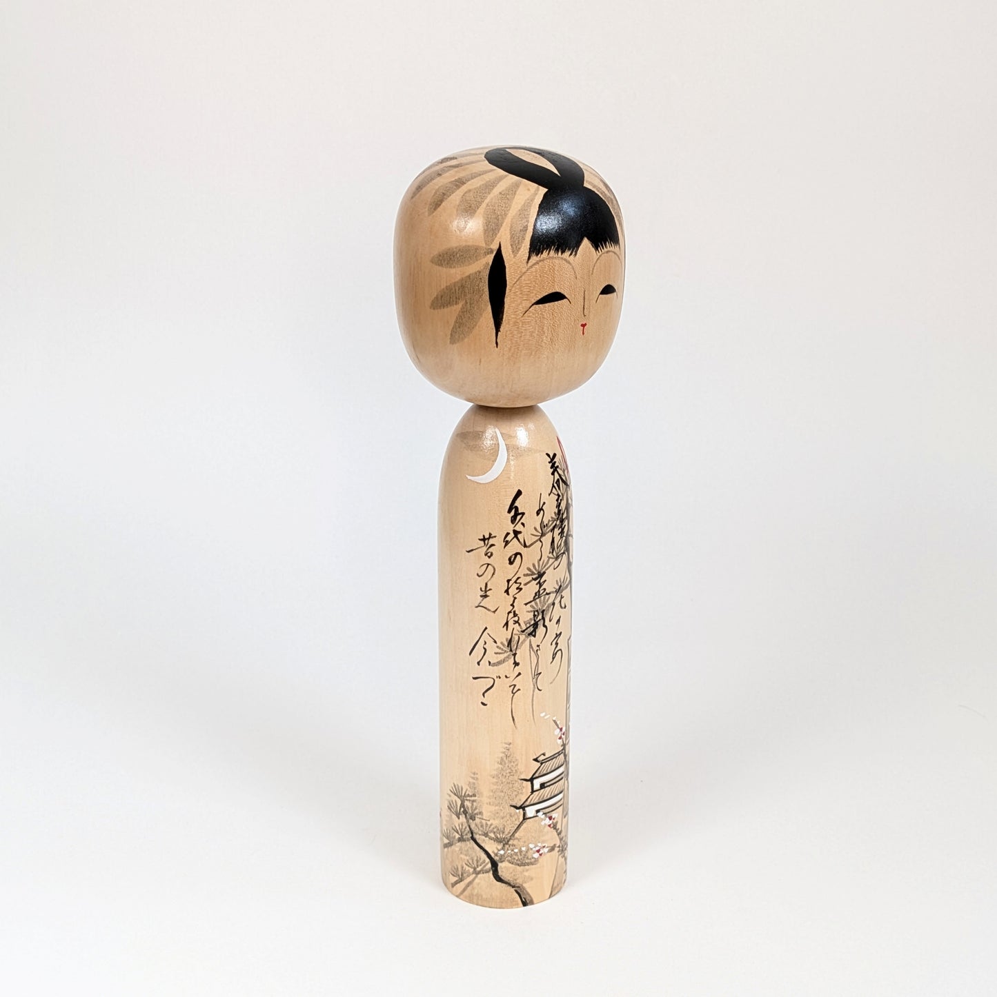 Poupée japonaise en bois signée Shūhō, vue trois quarts avec calligraphie, lune et décor architectural japonais.