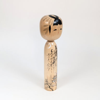 Poupée japonaise en bois signée Shūhō, vue trois quarts avec calligraphie, lune et décor architectural japonais.
