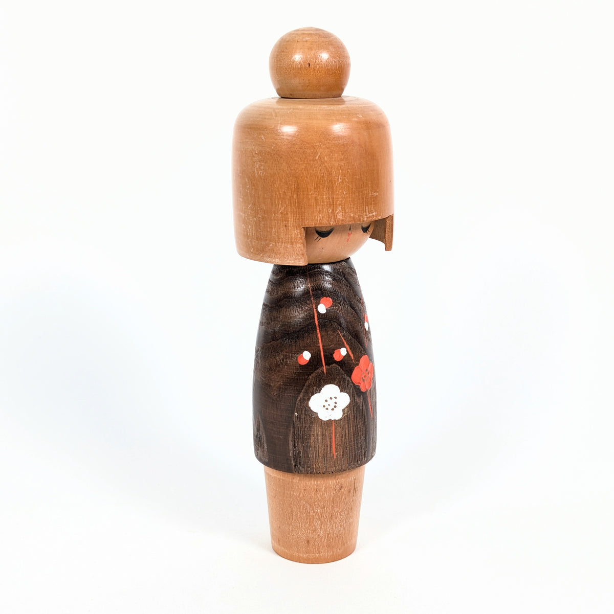 Poupée japonaise en bois Koigokoro par Usaburo, vue de trois quarts révélant sa coiffure sculptée, son visage aux yeux clos et son kimono à motifs floraux.
