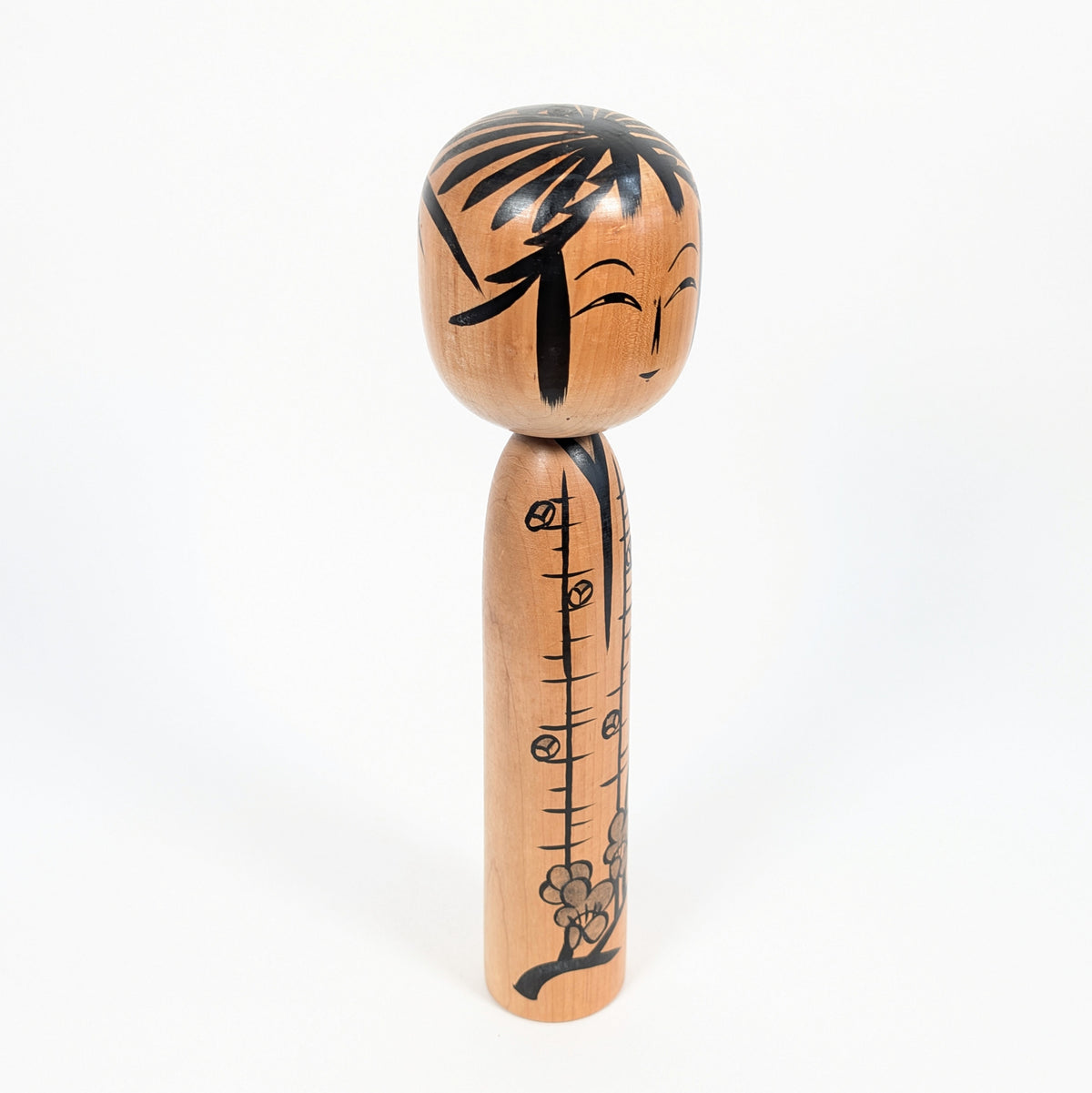 Poupée kokeshi ancienne en bois naturel, vue de trois quarts, décorée de branches fleuries par l'artisan japonais Satō Yoshiaki.