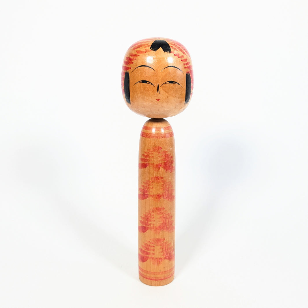 Vue de face d’une kokeshi traditionnelle Togatta signée Onuma Shoji, visage souriant, tête à motif tegara rouge et corps kasanegiku.