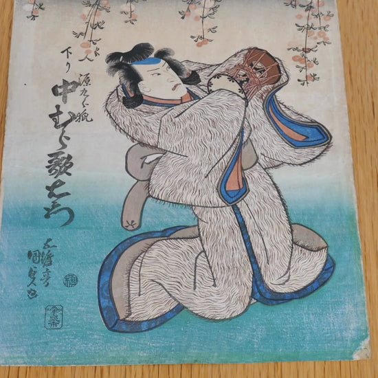 Estampe de 1838 signée Kunisada, représentant l’acteur Nakamura Utaemon dans le rôle du renard Genkurô, issu de la pièce kabuki Yoshitsune Senbon Zakura. Le personnage tient le tambour Hatsune. Détails raffinés : kimono à motif "fourrure", cerisiers pleureurs en fleur, gaufrage karazuri visible. Couleurs patinées, coins abîmés. Belle pièce yakusha-e de la période Edo.