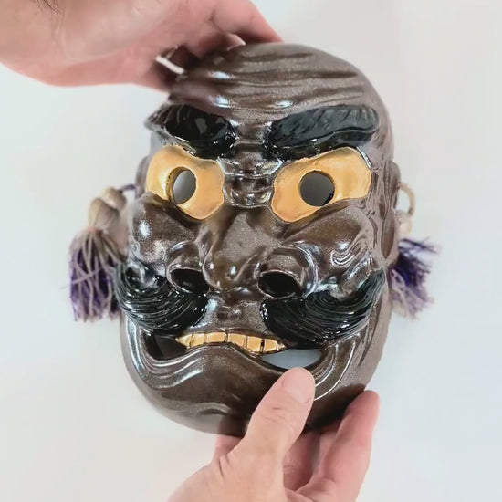 Vidéo de présentation du masque Nô japonais en céramique Kutani représentant Susanoo no Mikoto, signé Matsuda Sokawa, montrant les détails, reflets iridescents et cordelettes décoratives.