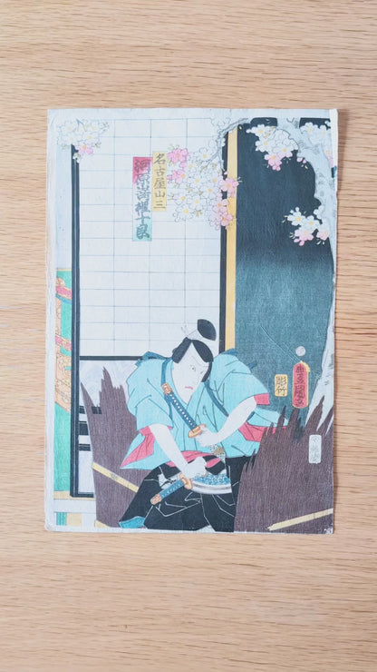 Vidéo détaillée d’une estampe japonaise originale de Kunisada Toyokuni III datée de 1861, représentant Kawarazaki Gonjuro I dans le rôle du samouraï Nagoya Sanza, avec sabres, costume kabuki, fleurs de cerisier, signature et sceaux.
