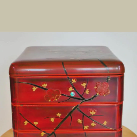 video de présensation d'une boite en laque Jubako en urushi rouge tournant sur un support. Elle présente des motifs de branches et fleurs de pruniers rouges. Maki-e et raden. Début 20ème siècle.