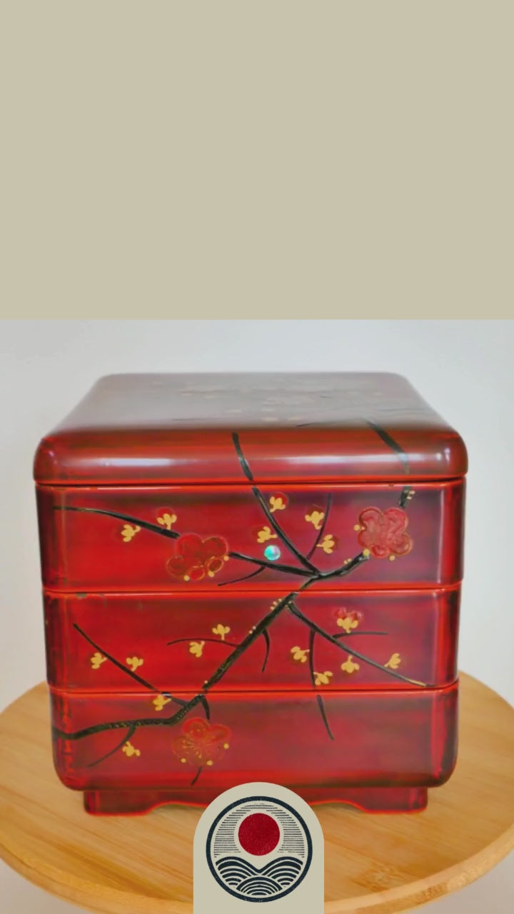video de présensation d'une boite en laque Jubako en urushi rouge tournant sur un support. Elle présente des motifs de branches et fleurs de pruniers rouges. Maki-e et raden. Début 20ème siècle.