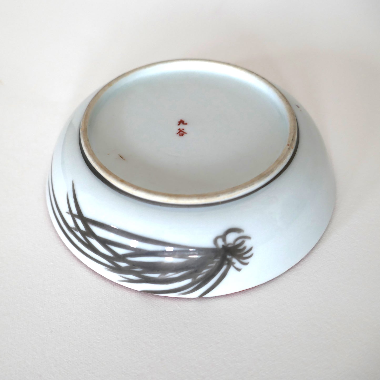 Revers d’une assiette Kutani signée 九谷 avec motif de pin stylisé en noir sur porcelaine blanche