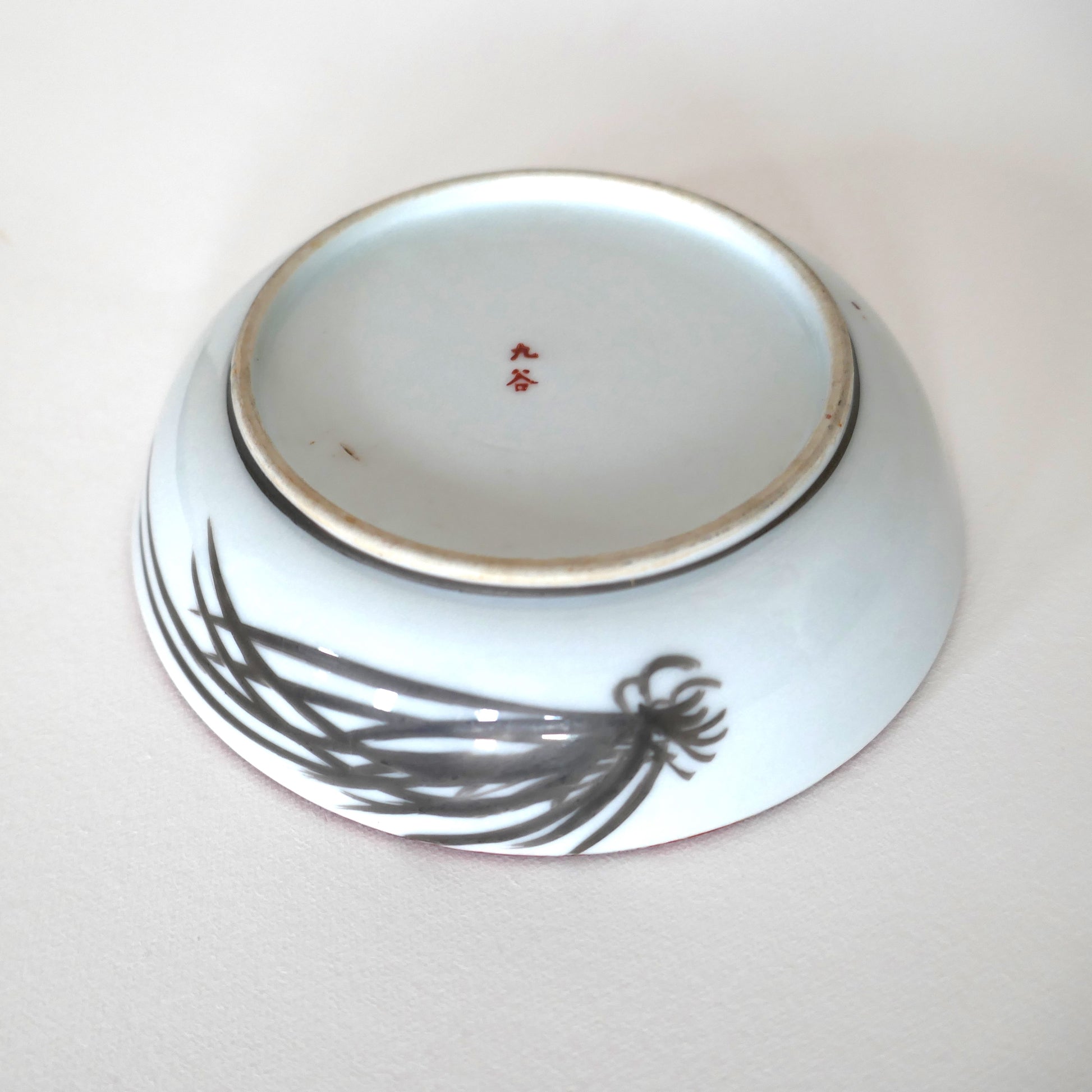 Revers d’une assiette Kutani signée 九谷 avec motif de pin stylisé en noir sur porcelaine blanche
