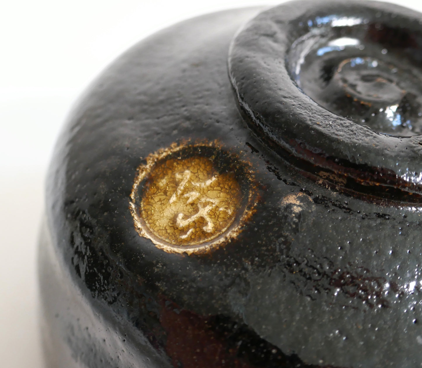Gros plan sur le cachet doré 光楽 sous le chawan raku, près du pied annulaire kōdai et de la marque du potier.
