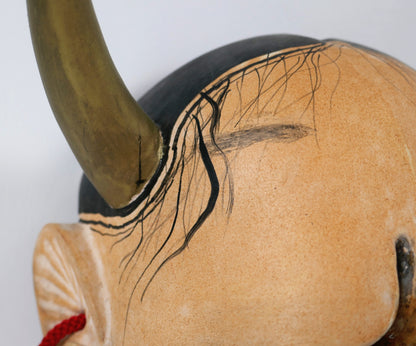 Détail d'une corne dorée de masque Hannya et des fines mèches noires peintes sur le front ivoire.