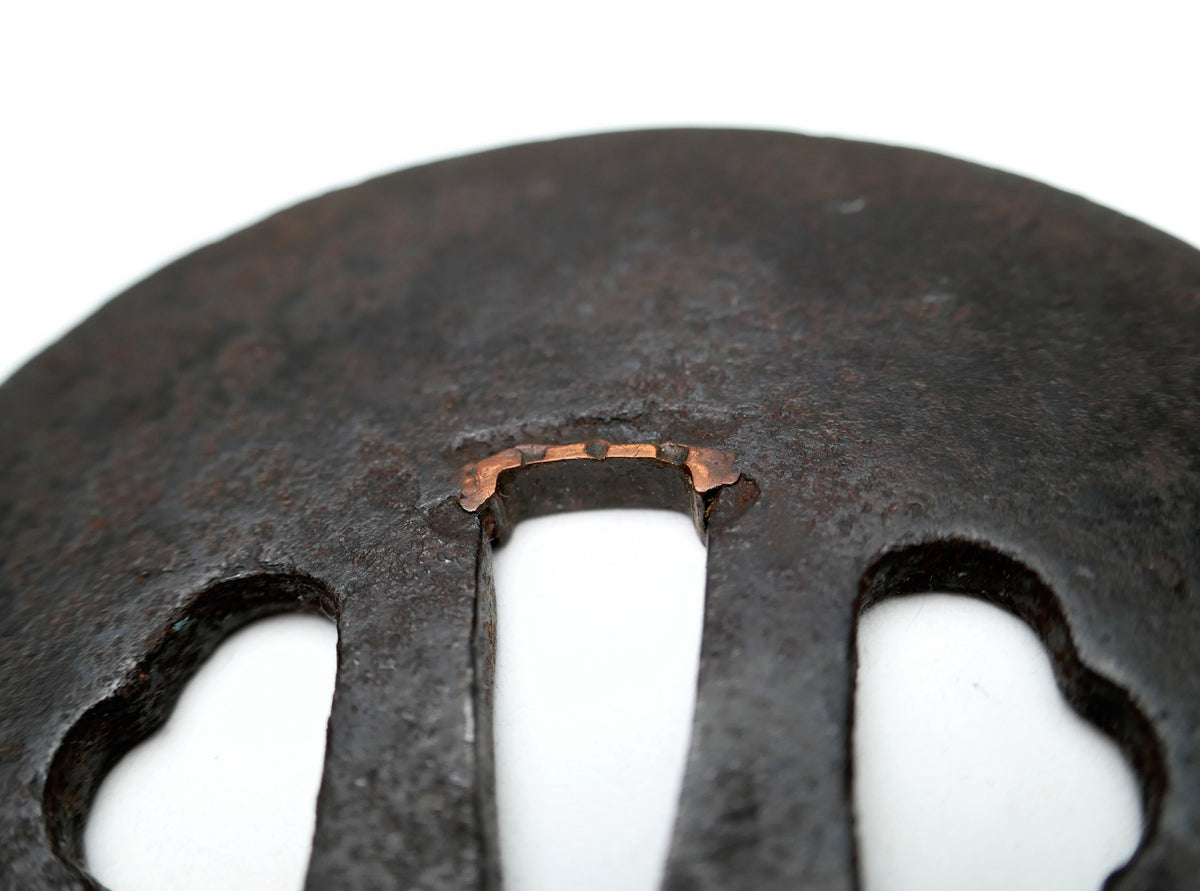 Gros plan des sekigane en cuivre ajustant le nakago-ana d’une tsuba japonaise antique en fer, ancienne garniture de nihontō.