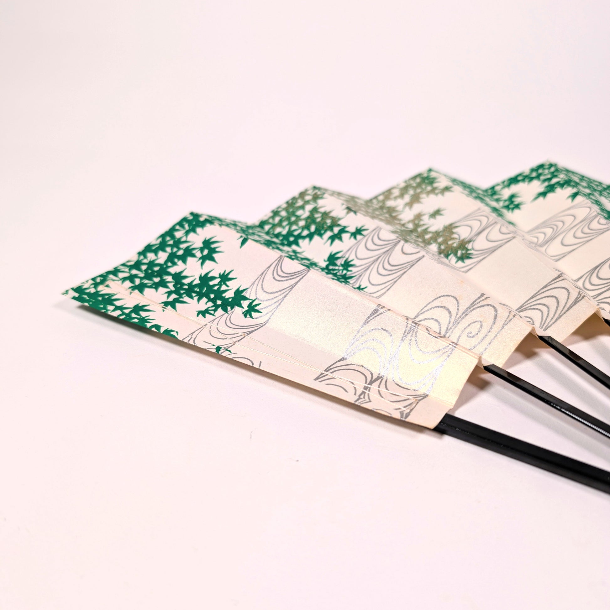 Détail du papier nacré d’un sensu japonais avec feuilles d’érable vert et lignes d’eau courante gris argenté.